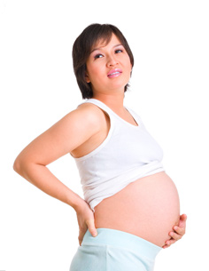 一名穿著白色背心的孕婦右手扶著後腰，左手撫摸著懷孕的大肚。